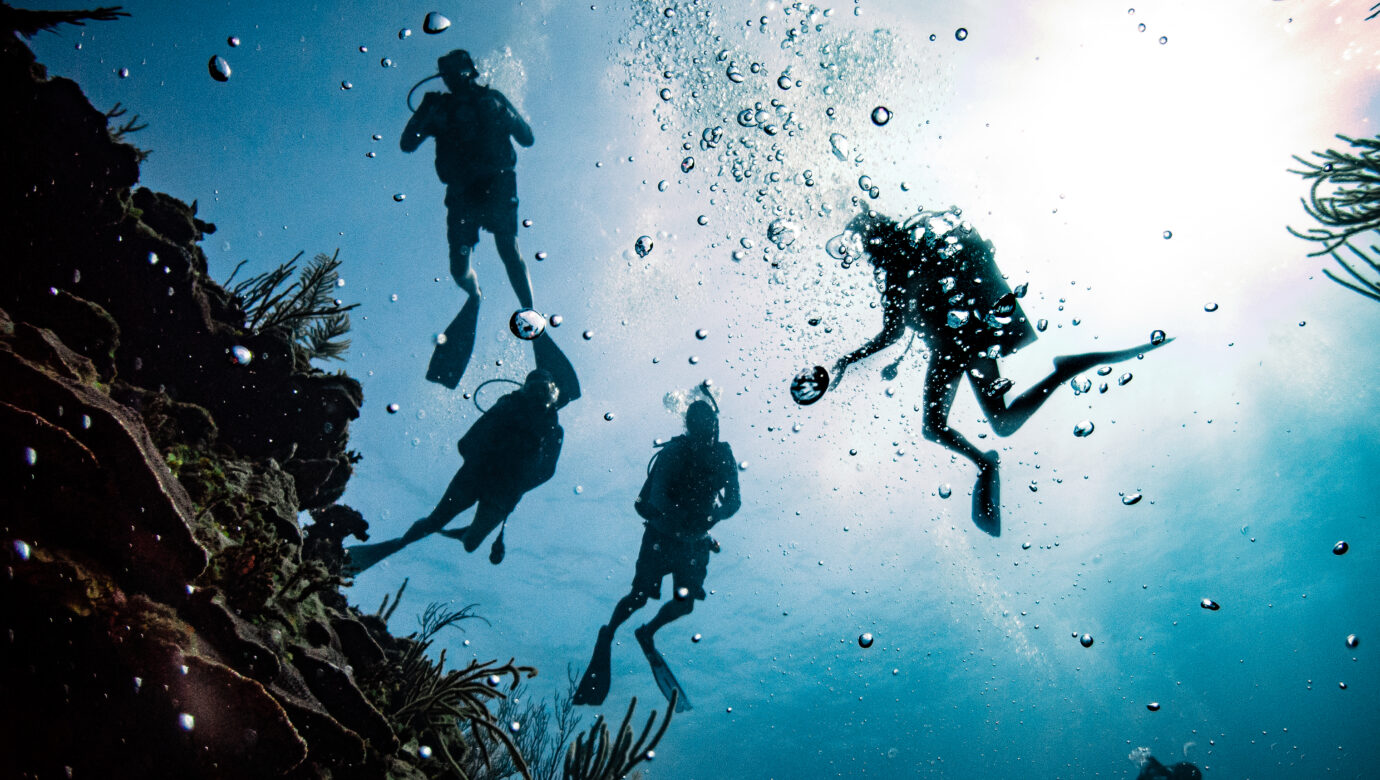 Group of divers in silhouette over the reef in San Pedro Belize photographed by Belize dive photographer Will Blochinger