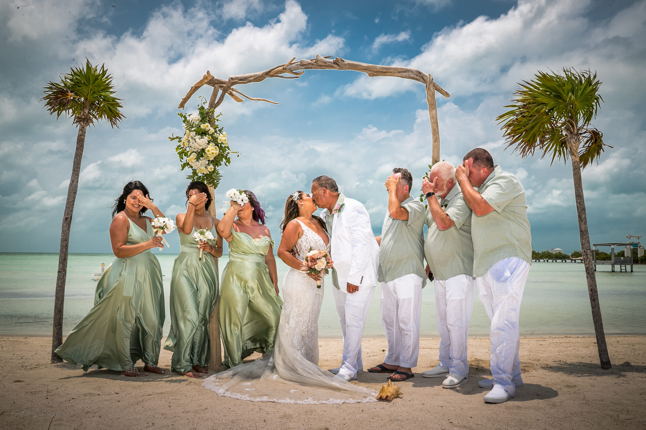Bride and groom kissing with wedding party on the beach by the Caribbean Sea at Mahogany Beach San Pedro Belize photographed by belize wedding photographer Will Blochinger