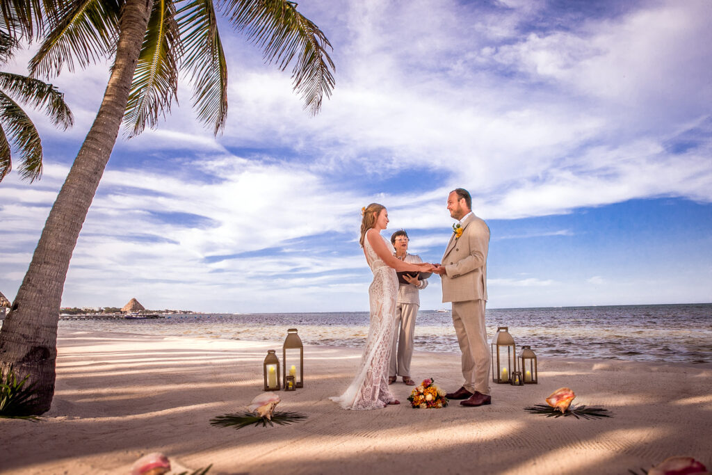 Bride and groom holding hands during a beach wedding ceremony beneath a palm tree in San Pedro, Belize