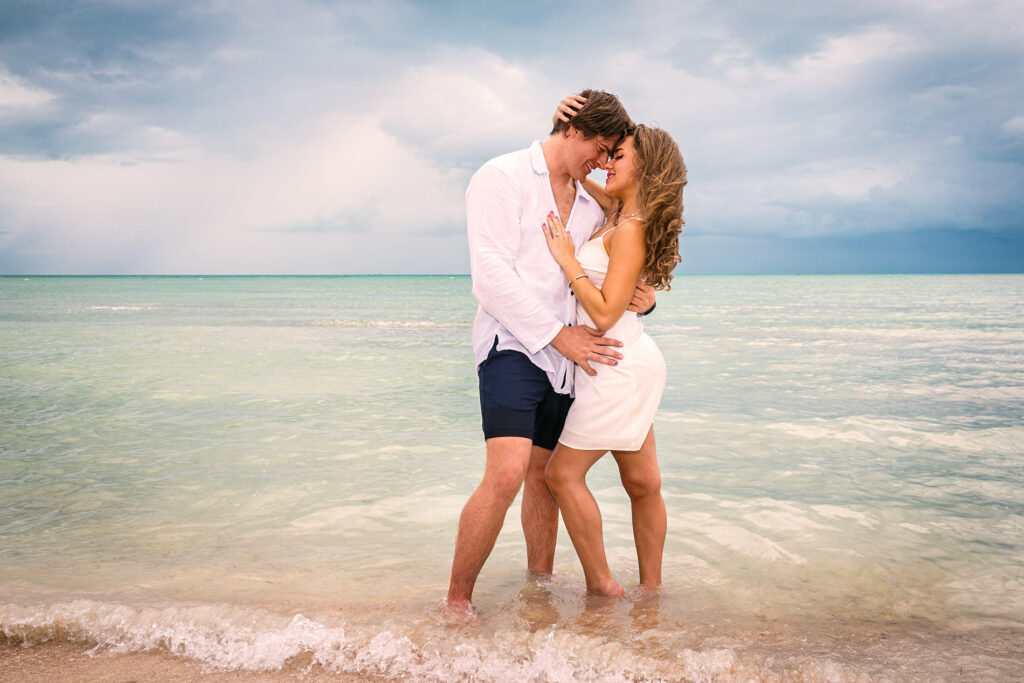 Couple embracing barefoot in shallow turquoise water during a beach portrait session in San Pedro, Belize